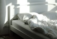 The sleep chart everyone copies has a footnote nobody reads An empty bed and floor lamp in morning sunlight