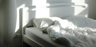 The sleep chart everyone copies has a footnote nobody reads An empty bed and floor lamp in morning sunlight