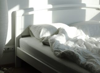The sleep chart everyone copies has a footnote nobody reads An empty bed and floor lamp in morning sunlight