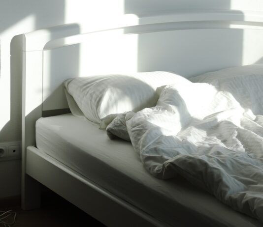 The sleep chart everyone copies has a footnote nobody reads An empty bed and floor lamp in morning sunlight