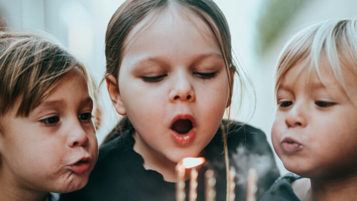 Two young children blowing out candles on a birthday cake