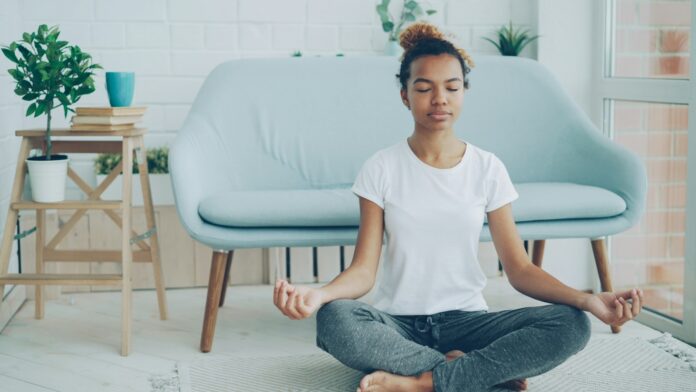 meditation-at-home A young woman sitting cross-legged meditating on the floor at home